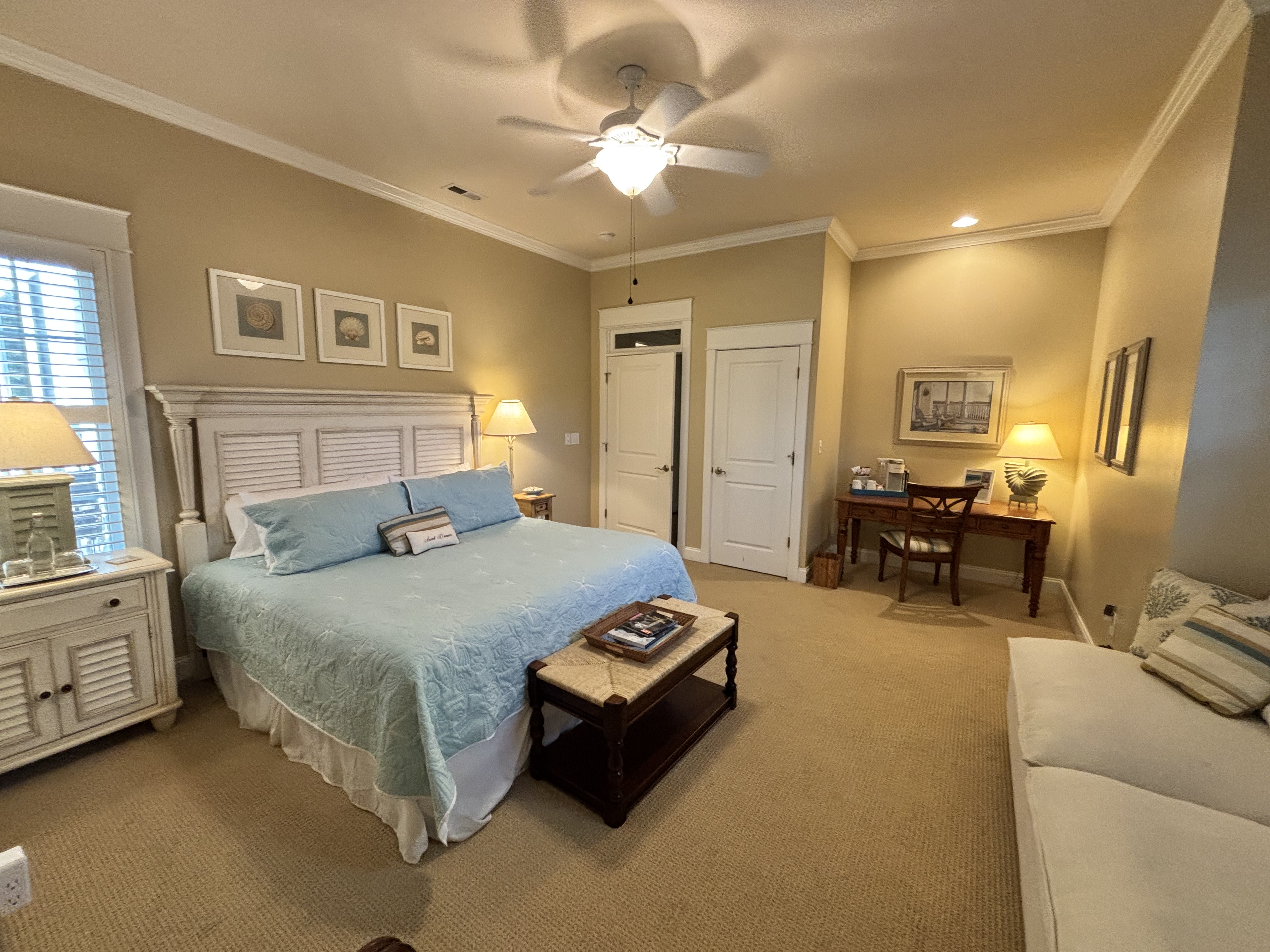 "Elegant guest room with king bed, light blue bedding, and beach-inspired décor. Features a writing desk with coffee station, cozy sitting area, and warm ambient lighting - perfect for a relaxing coastal getaway or bed and breakfast stay.
