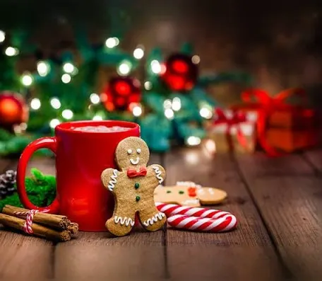 A red mug filled with hot beverage beside gingerbread men and candy, set against a festive background.
