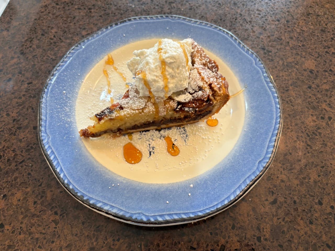 A slice of cake topped with whipped cream and drizzled with caramel, served on a blue plate.