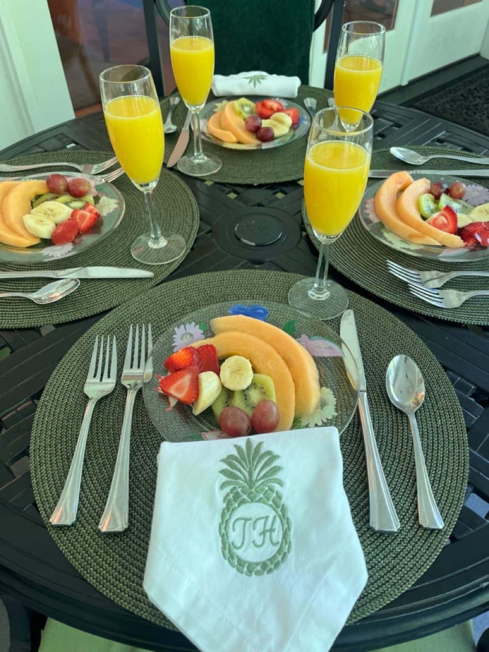 A stylish outdoor breakfast table set with plates of fresh fruit and mimosas.