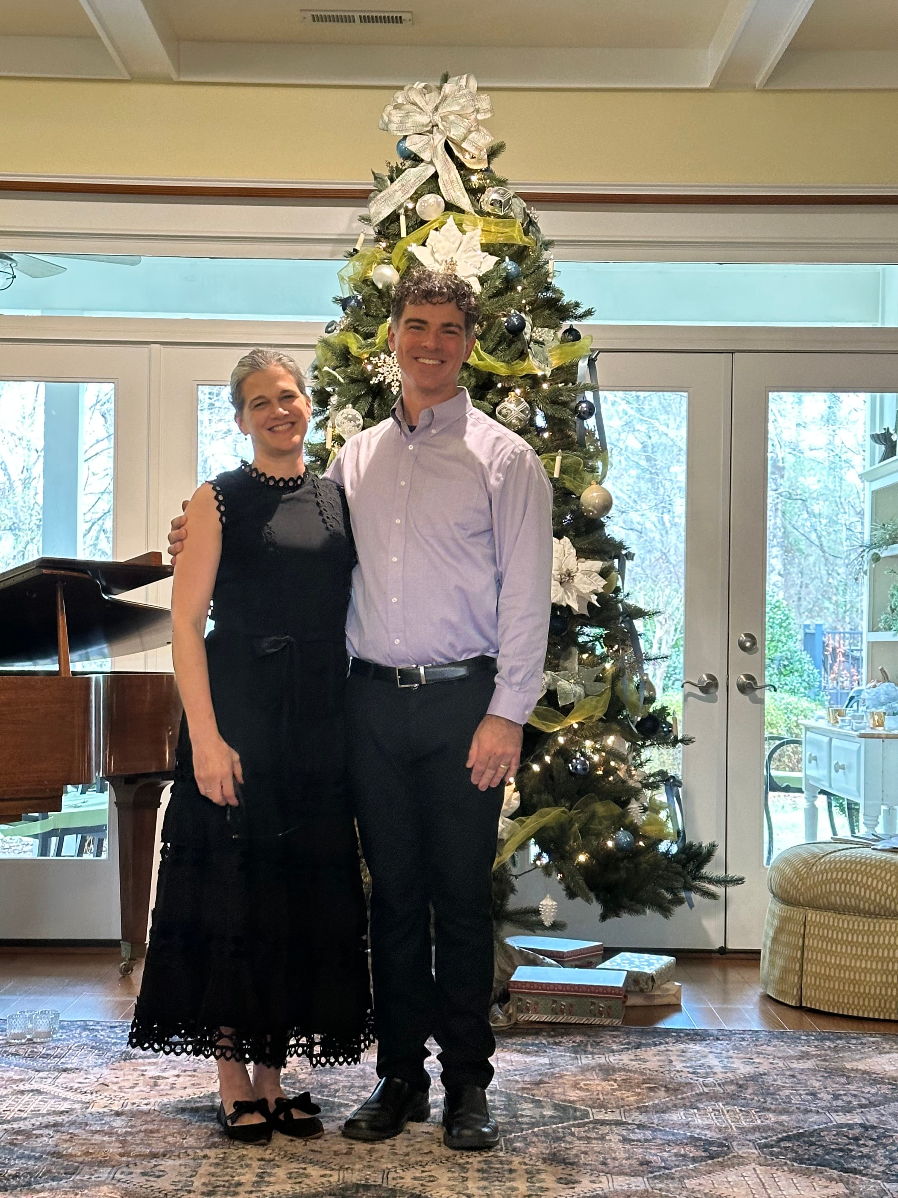 A man and woman pose together in front of a decorated Christmas tree.