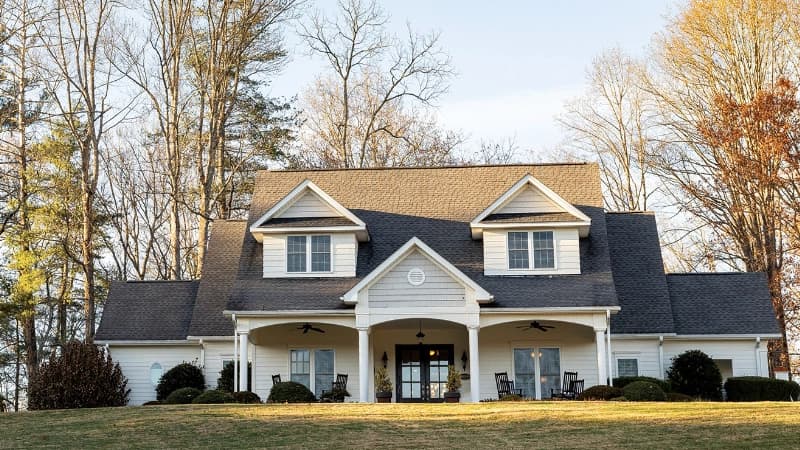 A large, white house with a dark roof and front porch, surrounded by trees.