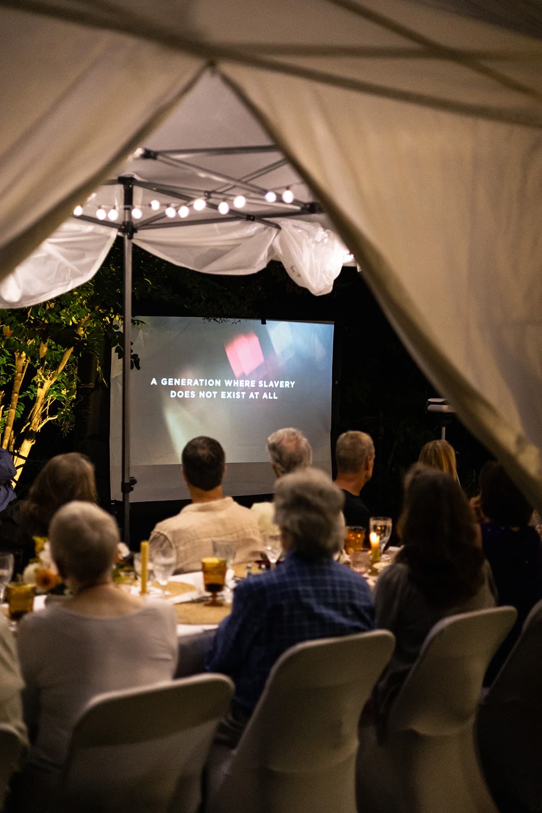 A group of people seated at a dinner table watches a film projected on a screen displaying the message about a future without slavery.
