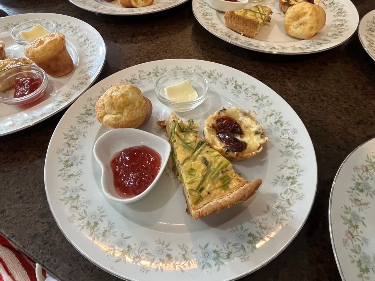 A delicate plate featuring quiche, a savory tart, muffins, jam, and butter.
