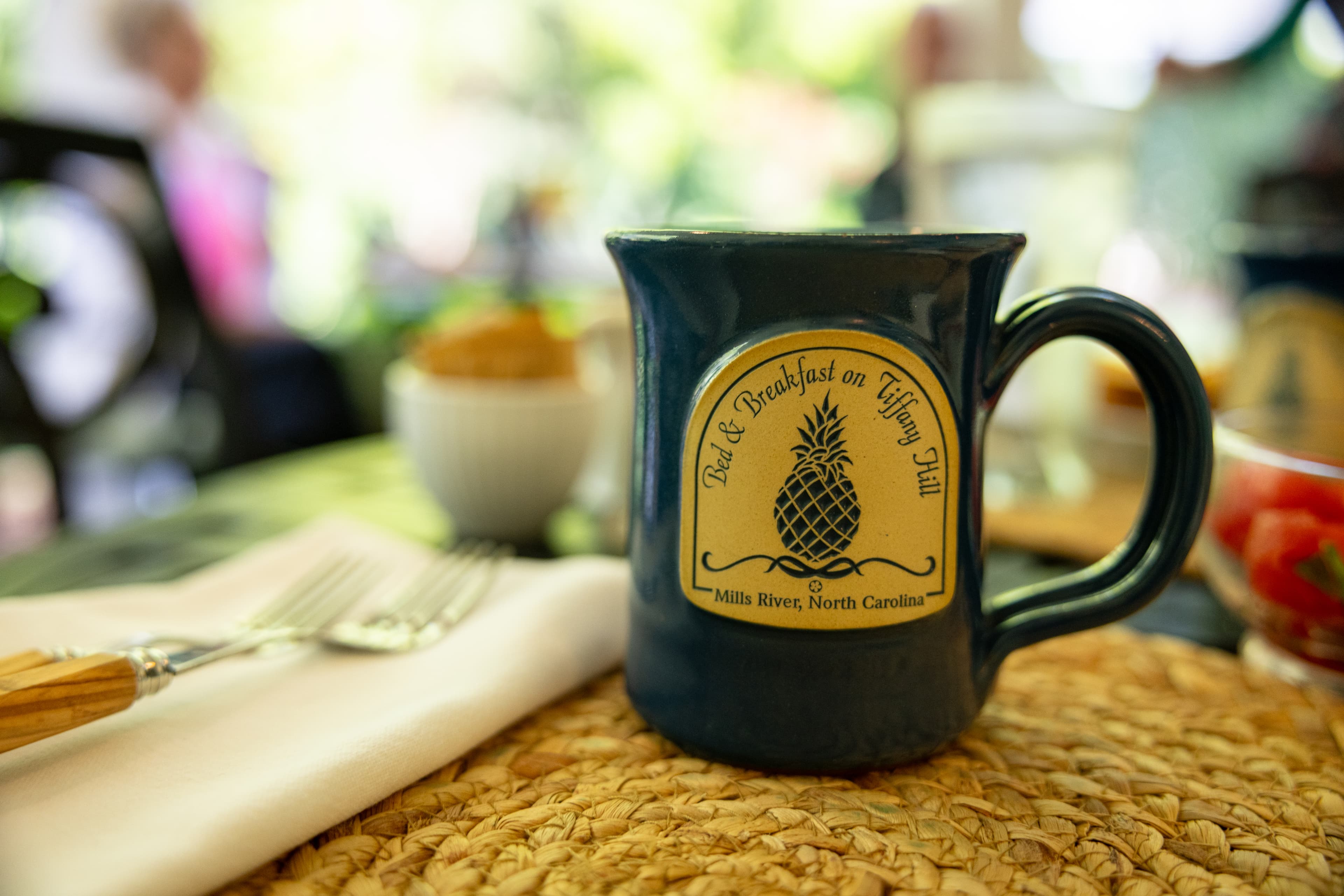 A ceramic mug with with logo and name of a bed and breakfast on a wicker breakfast mat