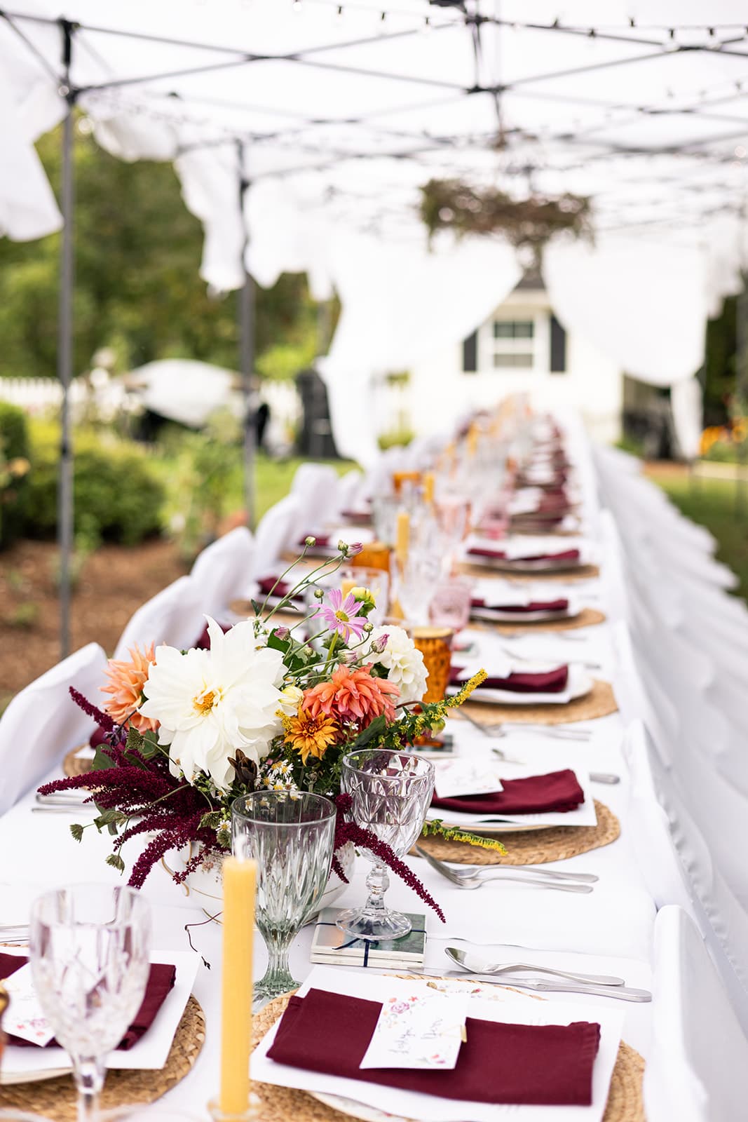 A beautifully arranged long dining table under a canopy, featuring floral centerpieces and elegant table settings.