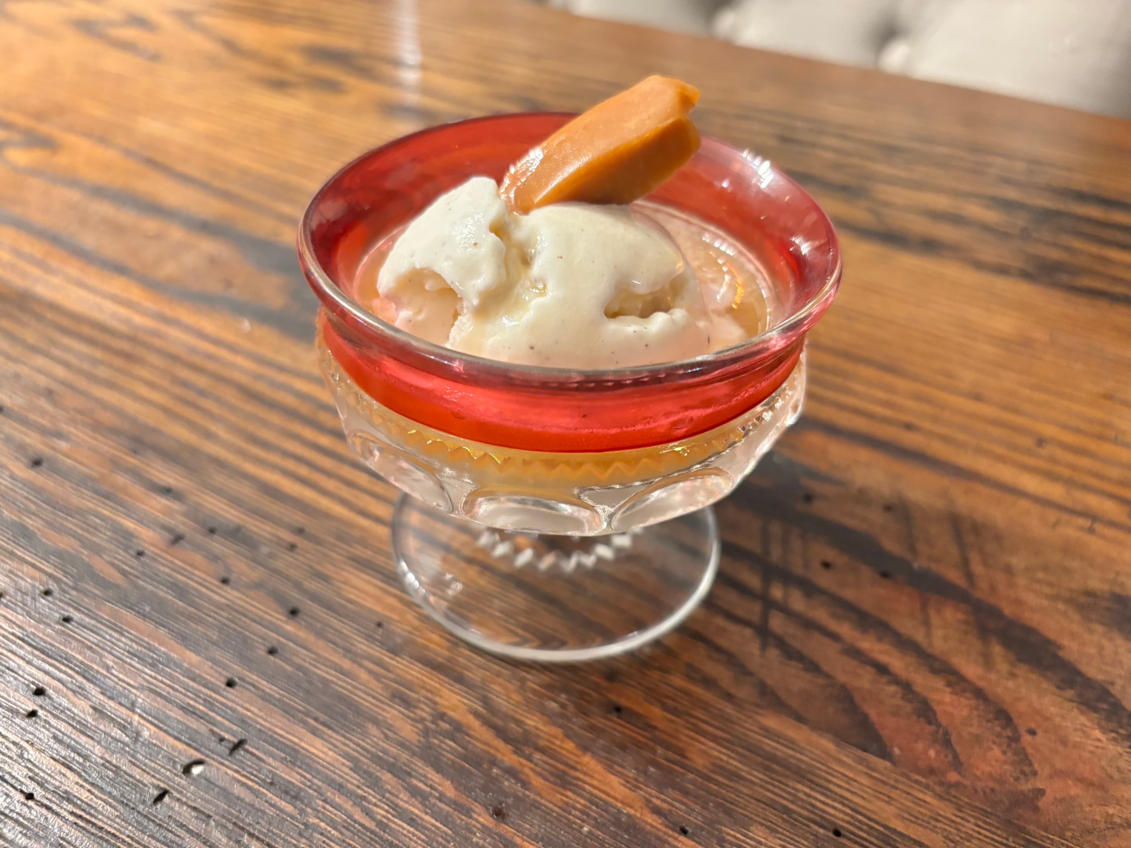 A small glass dessert dish filled with creamy ice cream topped with a caramel sauce and a piece of caramel candy.
