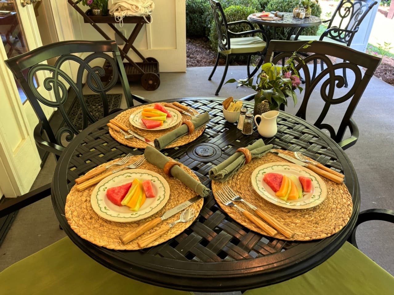 A beautifully arranged outdoor table set with fruit plates, utensils, and napkins.