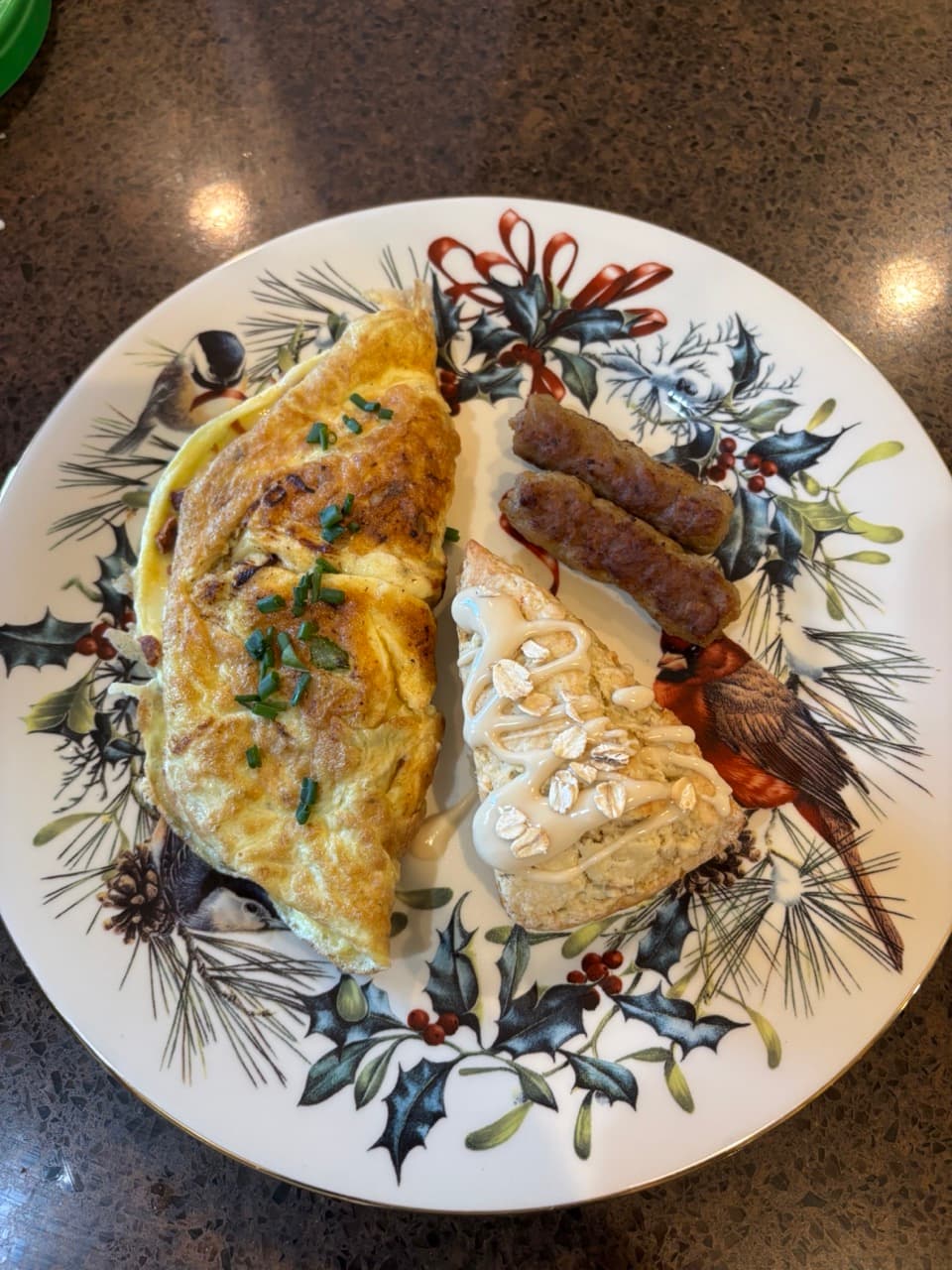 A plate featuring a chive-topped omelette, two sausage links, and an oatmeal scone drizzled with icing, set against a festive holiday background.