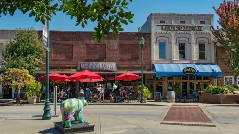 A colorful cow sculpture stands on the sidewalk in front of outdoor dining at Mezzaluna and Black Rose Pub.